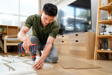 Man assembling purchased furniture in beautiful room with large window. Concept of DIY or furniture assembly services
