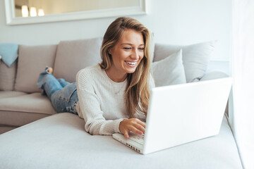 Fototapeta premium Happy Woman Lying on Couch Using Laptop at Home for Online Work and Relaxation