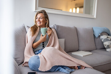 Cozy Morning On Sofa: Woman Smiles While Sipping Tea With Mug, Blanket, And Laptop Nearby