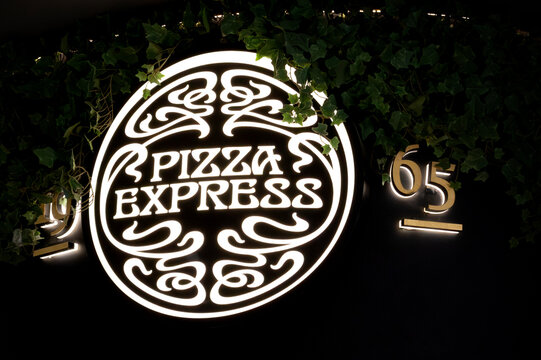 London, UK - December 18 2025: Illustrative editorial PizzaExpress logo restaurant sign illuminated at night with ivy foliage