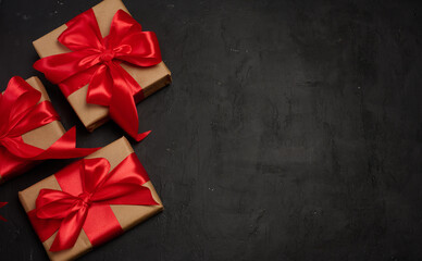 A gift box wrapped in craft paper and tied with a large bright red satin bow on a black background.
