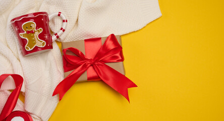 Christmas composition: two gift boxes with red bows, a mug and a Santa hat on a yellow background.
