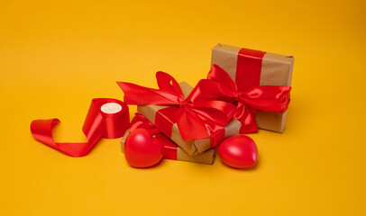 Gifts wrapped in brown paper and red satin ribbon on a yellow background, holiday