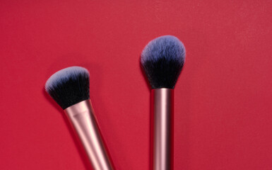 Two makeup brushes with lilac bristles on a red background, top view