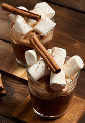 A glass of hot chocolate with fluffy marshmallows on a wooden table.