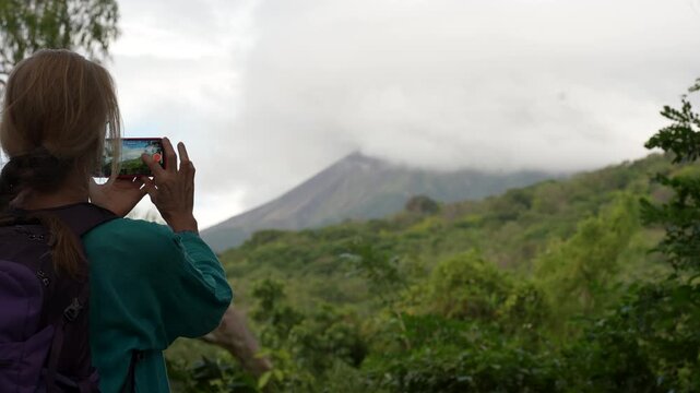 A mature woman enjoys hiking in Charco Verde park on Ometepe Island, Nicaragua while taking pictures of the landscape and volcano.