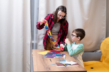 A young woman in a red plaid shirt makes a paper garland for Christmas with her son, who uses hearing aids. DIY Christmas home decor.