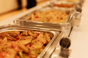 Several metal trays filled with different food options are set up on a table at a gathering in a...
