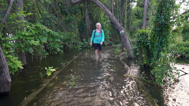 Mature woman hikes through water in Charco Verde park on Ometepe Island in Nicaragua surrounded by jungle scenery and nature.