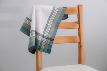 A folded white handkerchief with green and grey stripes is draped over the wooden backrest of a chair.
