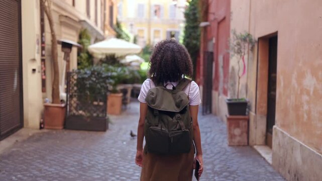 Young female traveler with backpack walking narrow historic street in Rome Italy, exploring old town architecture and cozy urban atmosphere during relaxed city holiday travel