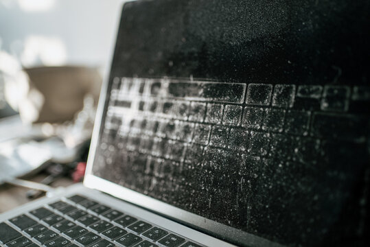 Old laptop showing heavy dust and grime accumulation on its black screen and keyboard, concept of abandonment, neglect, outdated technology, and a forgotten device