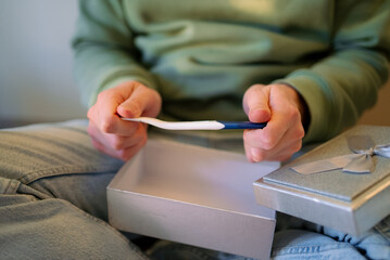 Person holding a white and blue pregnancy test, revealing exciting news about conception from an open silver gift box, symbolizing a joyous journey into parenthood with a surprise announcement