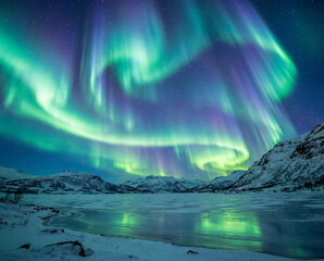 Naklejka premium Vibrant Aurora Borealis Over Snow Covered Mountains And Frozen Lake At Night