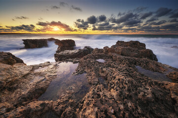 Sea waves during storm on sunset splash on stones.