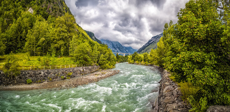 Fiume Dora Baltea (river) flowing through Aosta valley with mountains and cloudy sky