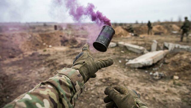 Soldier hands in camouflage uniform wearing gloves throwing a purple smoke grenade during military training or combat operation.