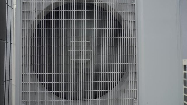 Outdoor air source heat pump unit with spinning fan behind protective grille. Concept of renewable heating, HVAC technology and energy efficient climate control system