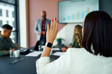 Confident young businesswoman raising hand to speak during team meeting in office boardroom