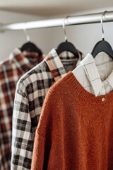 Several sweaters in different colors and patterns hang on wooden hangers in a neat row.
