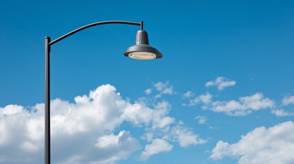Modern street lamp with pendant light against bright blue sky and fluffy white clouds, urban lighting design, architectural element, daytime scene