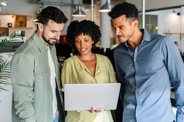 Three business colleagues reviewing laptop together during meeting. Professionals collaborating closely during a casual office discussion. Collaboration and planning concept.