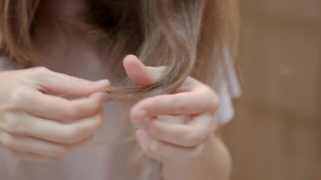 Close up of female hands holding and examining hair ends. Concept of hair care and split ends