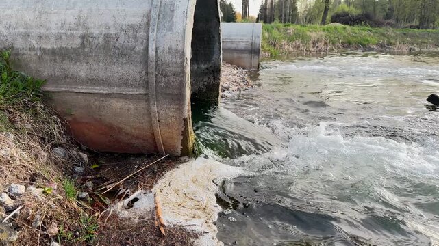 Concrete outfall pipe, discharging water or treated effluent into river or pond with foam and debris. Wastewater from sewage treatment plants, environmental concept