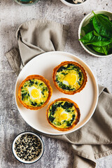 Eggs, spinach and cheese baked in tartlets on a plate on the table top and vertical view