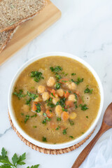 Chickpea carrot soup in a bowl with bread on white kitchen table. Top view.
