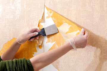 A woman is tearing old wallpaper off the wall.