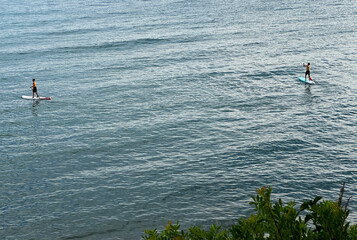 A calm blue sea with two surfers walking into the distance