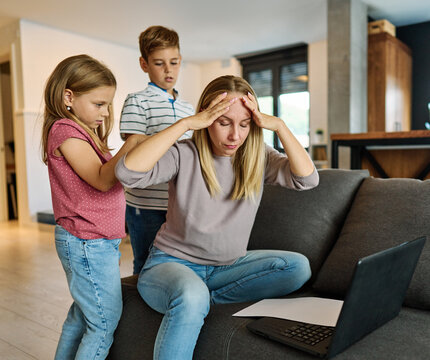 Portrait of a  business woman and a mother trying to work on a laptop when her little daughter and son  are playing, fooling around and interfering with her. Freelance, work from home, business office