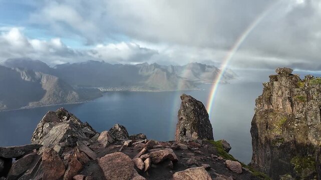 Breathtaking view of a double rainbow disappearing over a majestic Norwegian fjord from a rocky peak