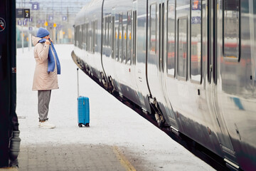 Quiet anticipation and inner readiness define the moment as a middle aged woman stands with a suitcase facing a train, capturing a calm pause before movement and change.