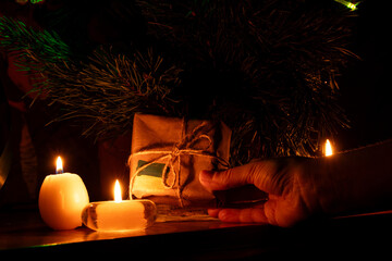 A New Year's tree and a woman's hand holding a gift wrapped in kraft paper with a Ukrainian flag by candlelight