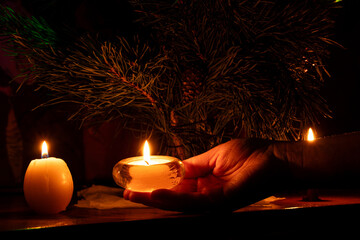 New Year tree and a woman's hand holding a candle near the tree in the dark