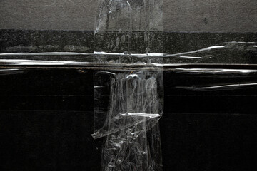 A black cardboard box tightly sealed with transparent adhesive tape in a crisscross pattern, close-up of the packaging surface, concept of delivery, protection
