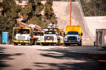 Utility trucks and portable toilet parked at construction site with trees and embankment © Tom Harwood