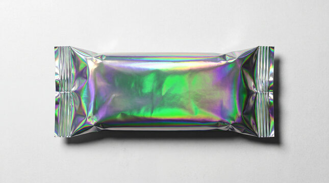 Blank holographic metallic foil snack bar wrapper mockup lying on a concrete surface with vibrant reflections for high energy food packaging design branding