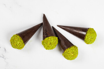 Dubai chocolate dessert. Dark chocolate cone with a ball of crispy kataifi dough with pistachio paste. White background. Close-up.
