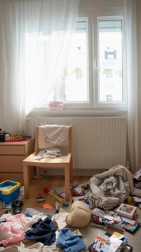 Messy children's bedroom with scattered clothes and toys on the floor. Disorganized chaotic interior with untidy pile of laundry and clutter vertical video.