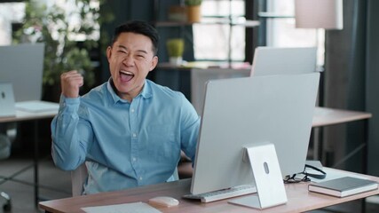 A young man sits at a desk in a stylish office, focused on his computer screen. Sunlight enters through large windows, creating a bright atmosphere.