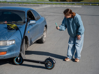 Woman examines and photographs the damage caused by a collision between an electric scooter and a car. © Михаил Решетников