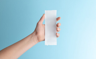 Hand holding blank paper receipt on blue background, minimalist mockup for expense documents, billing templates, refunds, and financial design concepts