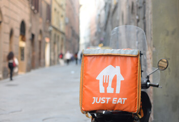 Naklejka premium SIENA, ITALY – OCTOBER 7, 2025: Just Eat food bag on parked scooter in the street. Just Eat is an online platform for ordering and delivering food founded in Danmark in 2001. Selective focus
