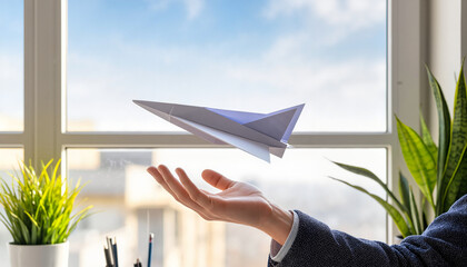 Businessman launching paper airplane from hand by window indoors  