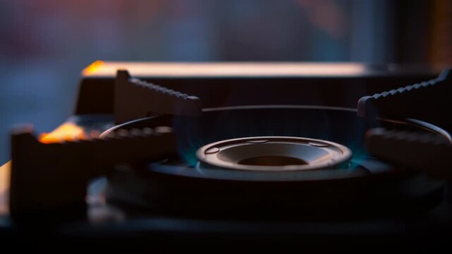 Portable gas stove burning with vivid blue flame, casting warm glow against shadowy background during evening twilight, highlighting compact cooking equipment's soft illumination