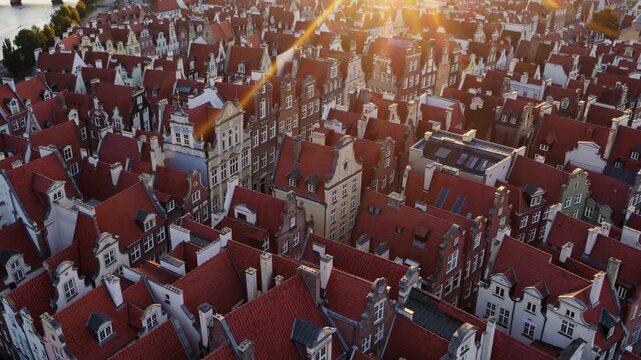 A vibrant cityscape showcases bustling rooftops adorned with red tiles, harmonizing beautifully under a golden sunset. Historic buildings with ornate details create a stunning urba