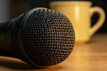 Close-up of a professional dynamic microphone on a wooden table with a blurred yellow mug, symbolizing audio and communication.